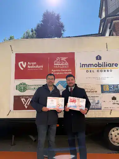 Due uomini sorridenti con certificati davanti a uno stand di Nebuloni Assicurazioni, sponsor evento.