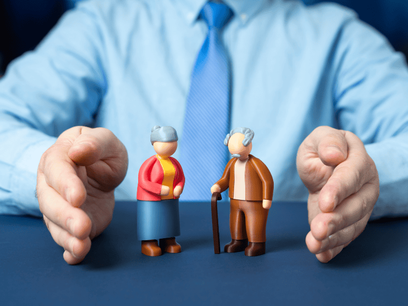 Due figure di anziani con assistenza, simbolo di protezione e cura assicurativa.